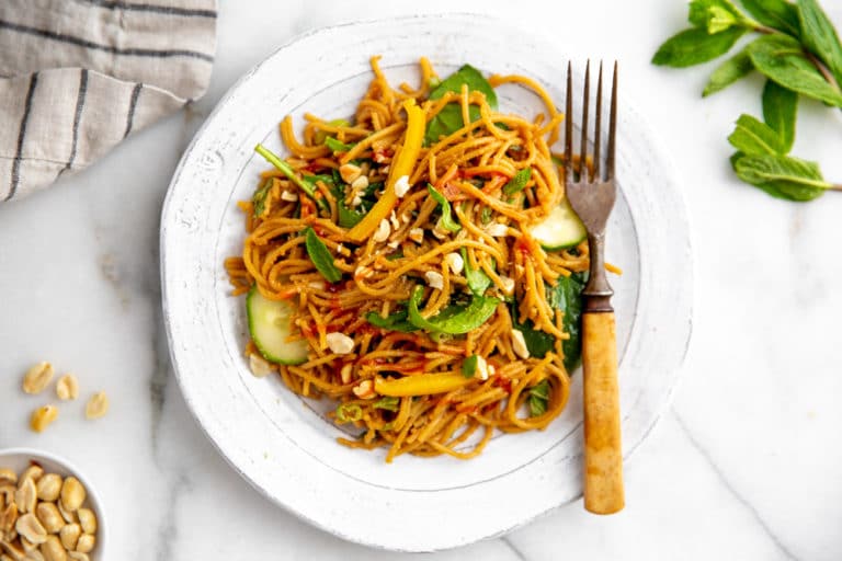 Overhead shot of cold Thai peanut noodle salad on a plate with a fork.