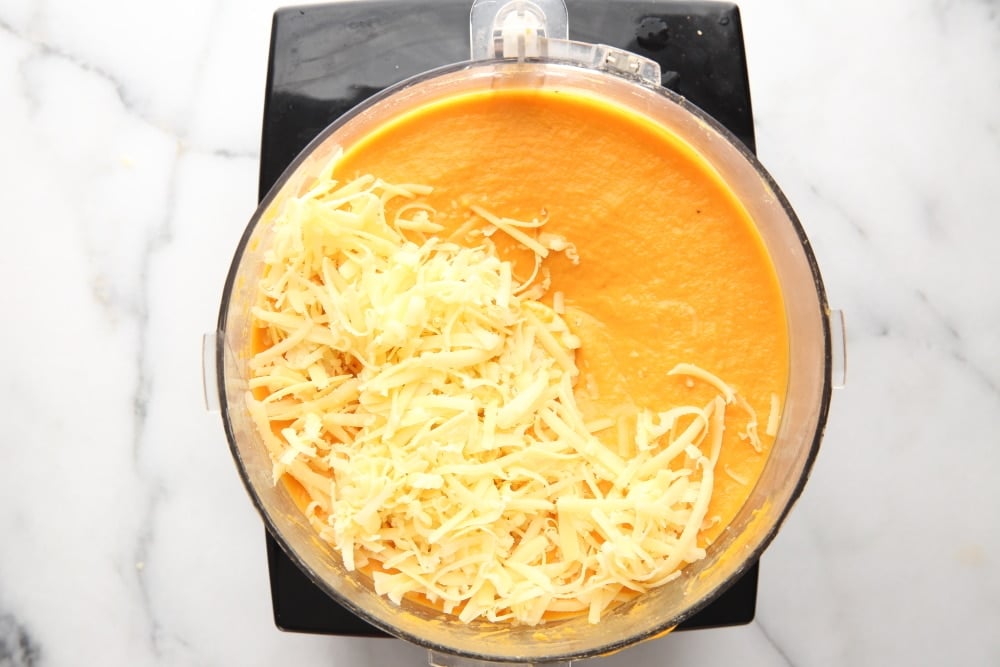 Process shot showing the whipped sweet potato souffle ingredients in food processor with cheese sprinkled on top.