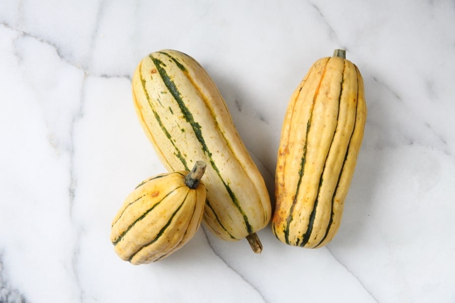 Three whole Delicata squash on a countertop. 