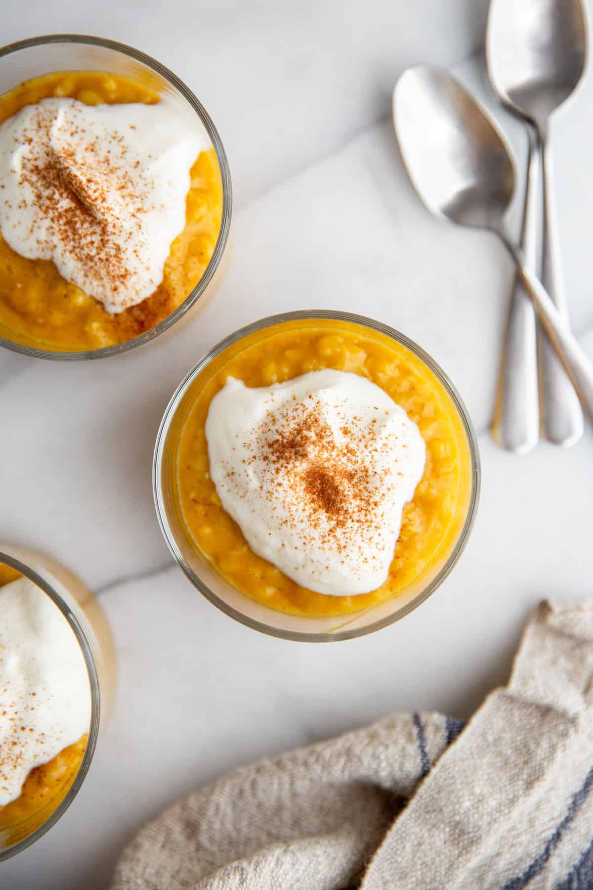 three jars of creamy pumpkin rice pudding on a counter topped with whipped cream and pumpkin pie spice