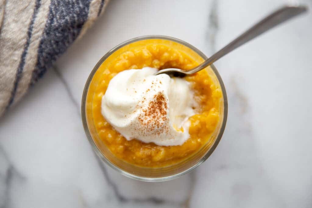 pumpkin rice pudding cooling in a jar topped with whipped cream and pumpkin pie spice