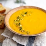 Vegetable potage soup in a bowl topped with chopped nuts, with cheesy baguettes alongside.