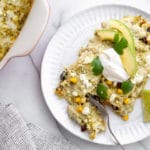 Salsa verde chicken enchiladas on a plate, topped with avocado and sour cream.