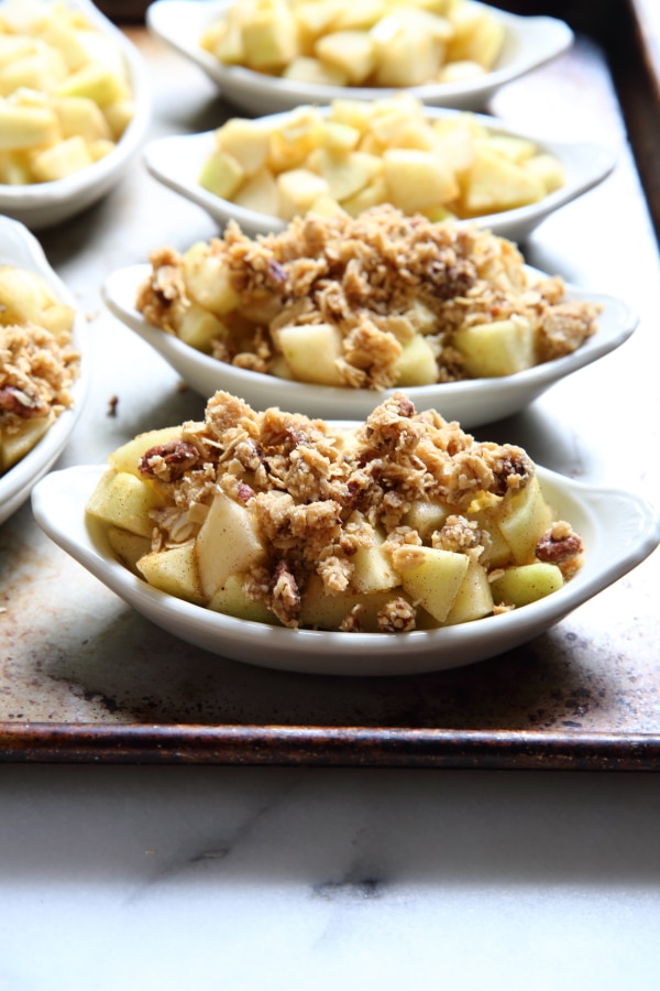 Unbaked apple crisps assembled in individual baking dishes. 