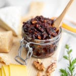 Fig chutney in a jar on a serving board with cheese alongside.
