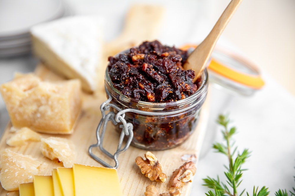 Fig chutney in a jar on a serving board with cheese alongside.