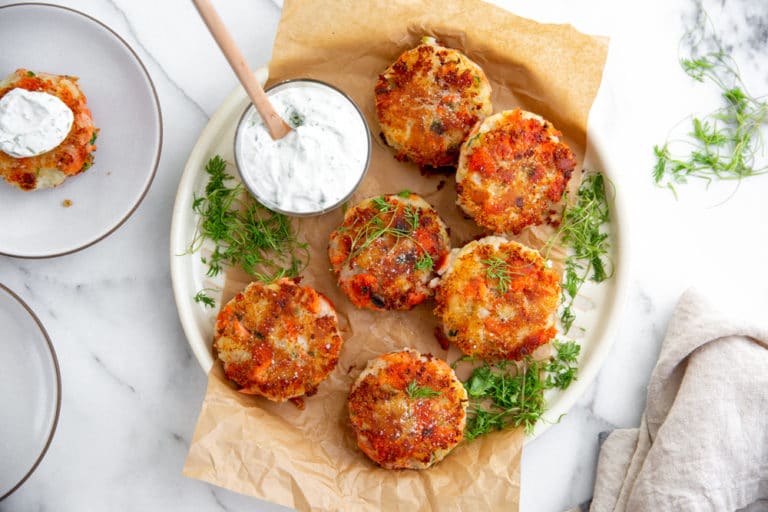 Salmon potato cakes on a platter with yogurt sauce alongside,