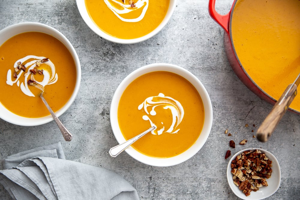 Overhead shot of bowls of healthy sweet potato soup on the countertop with a pot alongside.