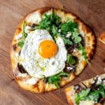 A mushroom flatbread pizza topped with a fried egg on a wooden board.