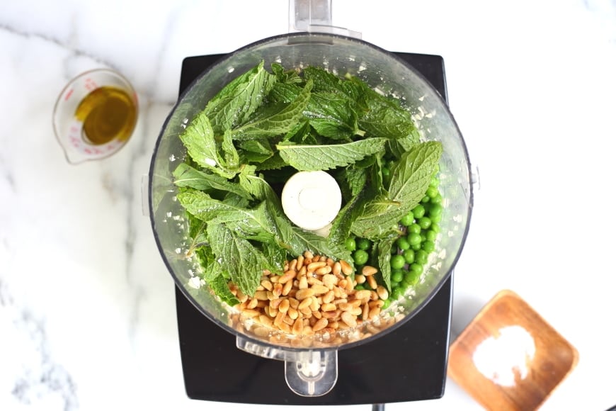 Process shot showing all of the ingredients for the pea pesto in a food processor.