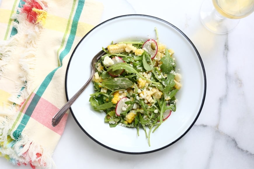 Overhead shot of sweet corn salad on table with glass of wine on the side