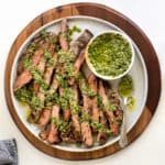 Sliced grilled skirt steak on a serving platter drizzled with salsa verde.