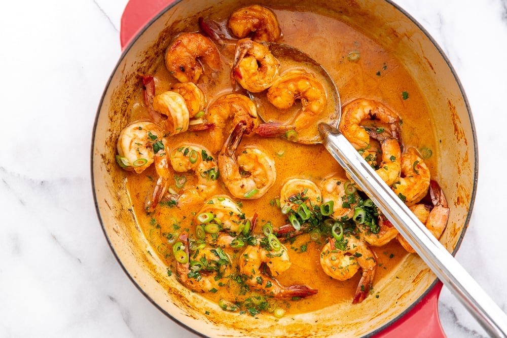 Shrimp in coconut sriracha sauce in skillet, with serving spoon