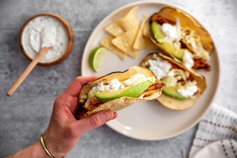 A taco in a hand, with a plate in the background