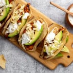 Easy chipotle chicken recipe served in tacos on a wooden cutting board with lime crema sauce on the side