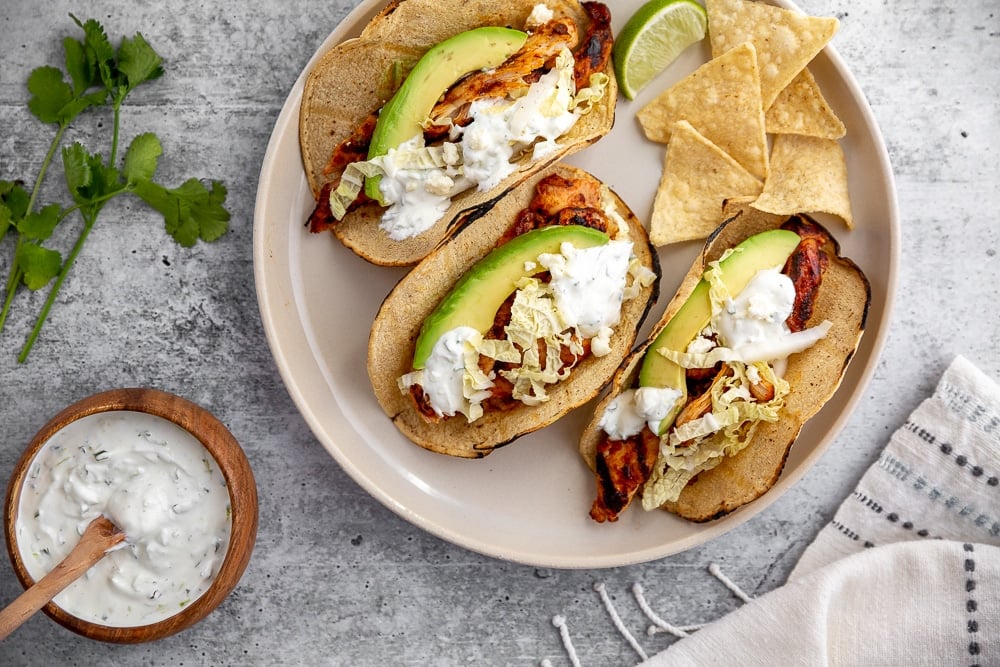 Tacos on a plate with tortilla chips and lime crema sauce on the side