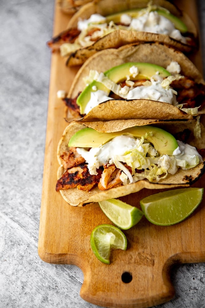 Easy chipotle chicken recipe in tacos, lined up on a wooden cutting board