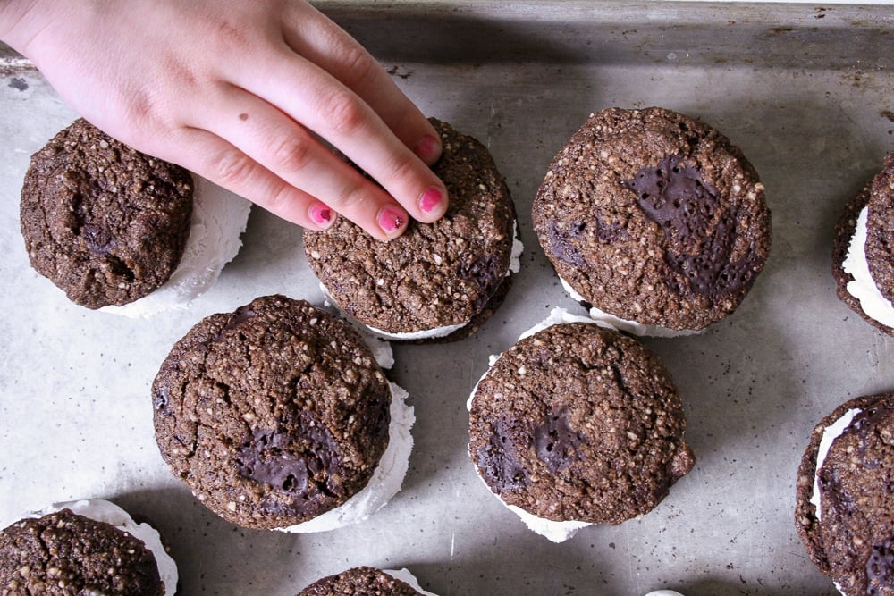 Hand grabbing vegan ice cream sandwich on sheet pan