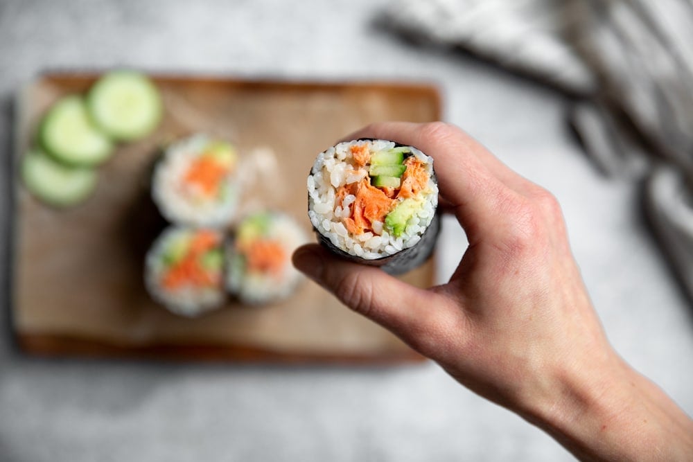 Hand holding a spicy salmon sushi burrito.