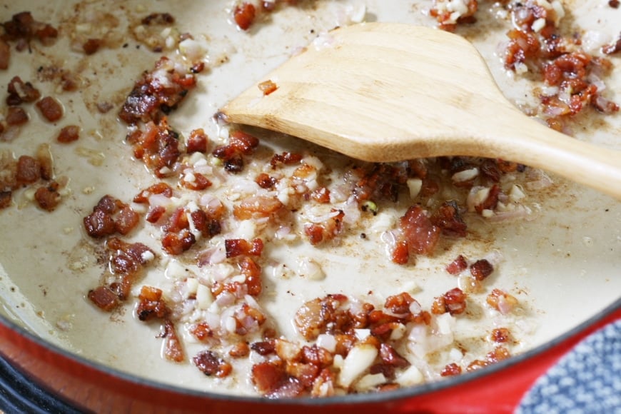 Crispy bacon cooking in a skillet with a wooden spatula
