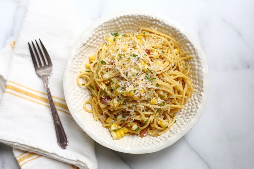 Overhead shot of a bowl of pasta with corn and bacon, with a fork alongside. 