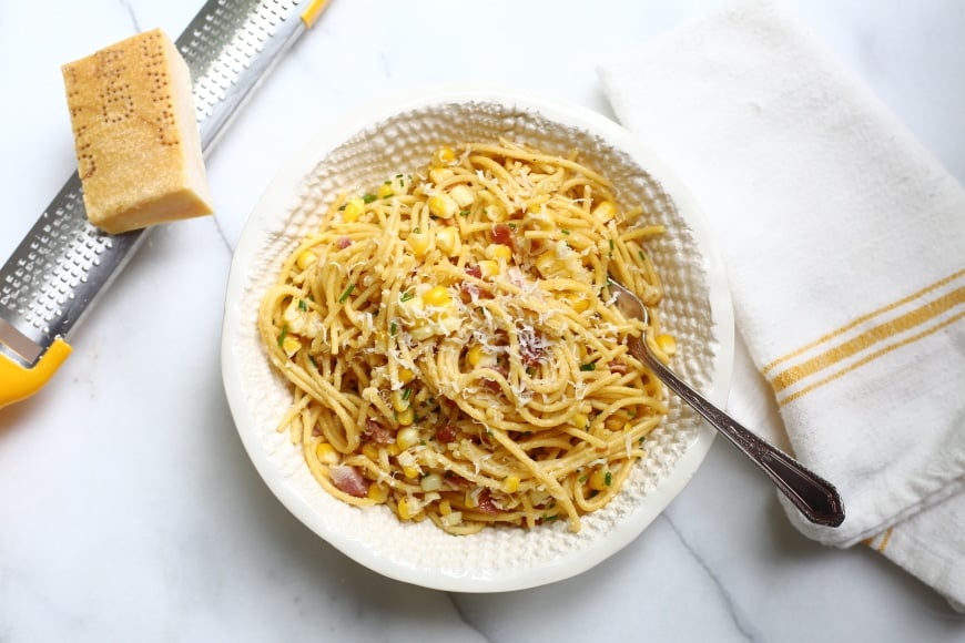 Overhead shot of bowl of spaghetti with corn and bacon, topped with with parmesan cheese.
