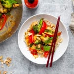 Healthy stir fry in a bowl with chopsticks, with a wok alongside.