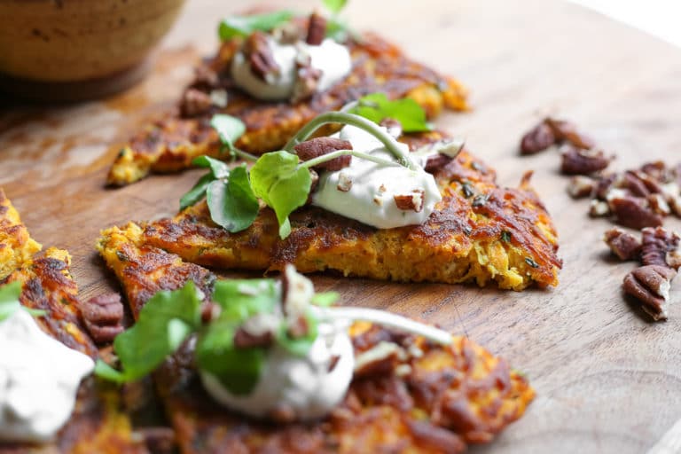 Close-up side view of a wedge of butternut squash latke cake topped with lime yogurt sauce.