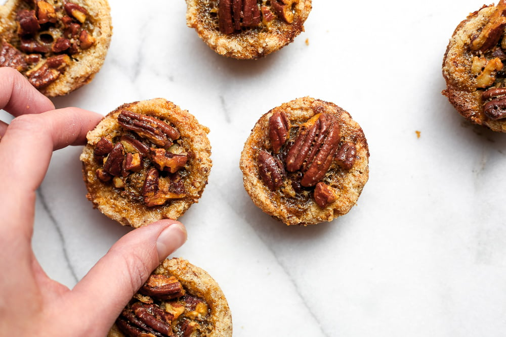 Hand grabbing a gluten free pecan tart off of a marble surface.