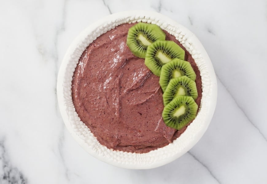 Process shot of adding fresh fruit to the top of the superfood berry smoothie bowl