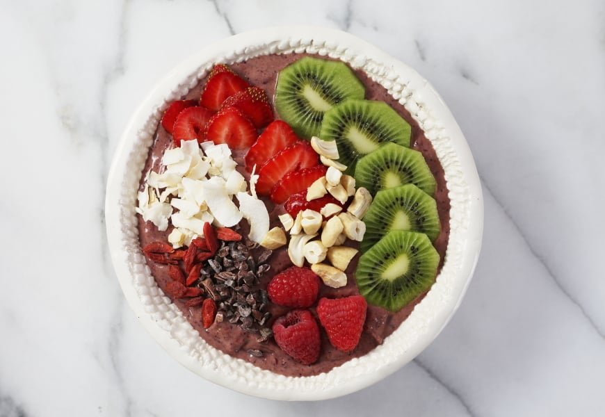 Superfood berry smoothie bowl topped with fresh fruit, cacao nibs, nuts and coconut