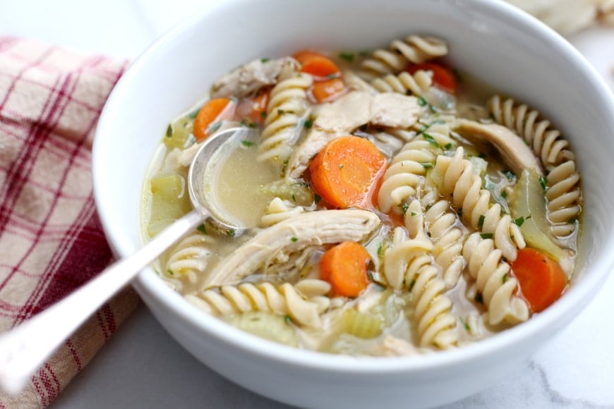 Close up of a bowl of chicken noodle soup with a spoon.