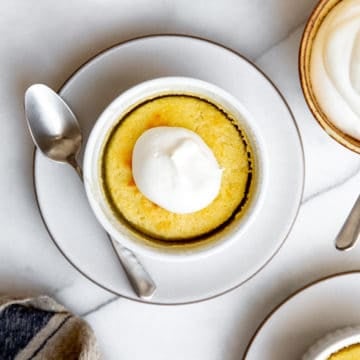 A lemon pudding cake on a plate dolloped with whipped cream.