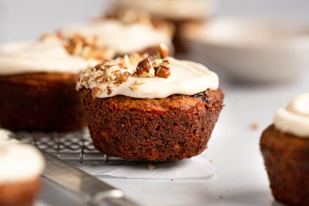 Close up of a carrot cake muffin topped with cream cheese frosting and chopped pecans.