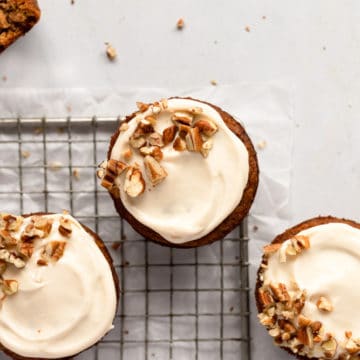 Gluten free carrot cake muffins with cream cheese frosting on a cooling rack.