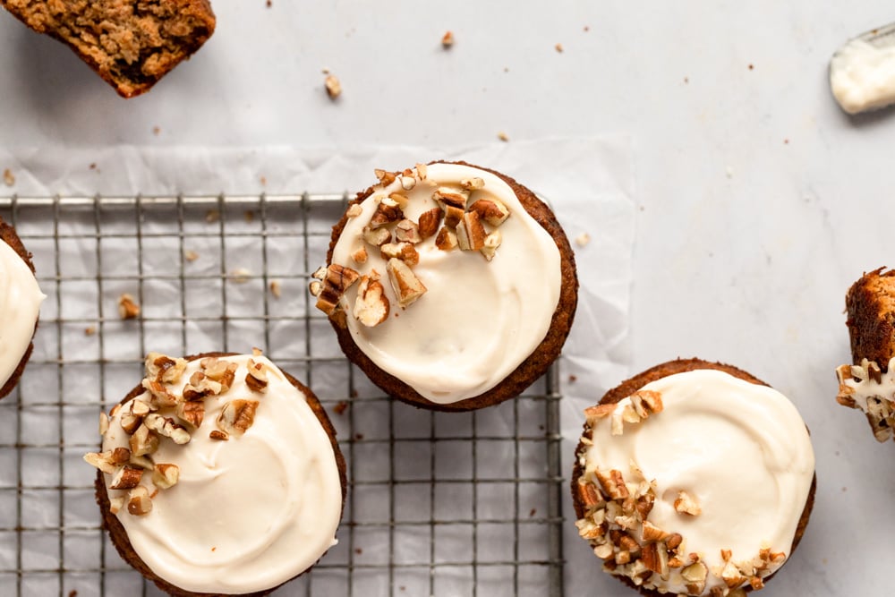 Gluten free carrot cake muffins with cream cheese frosting on a cooling rack.