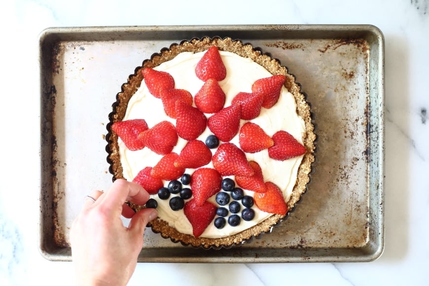 Process shot showing blueberries being arranged on tart.