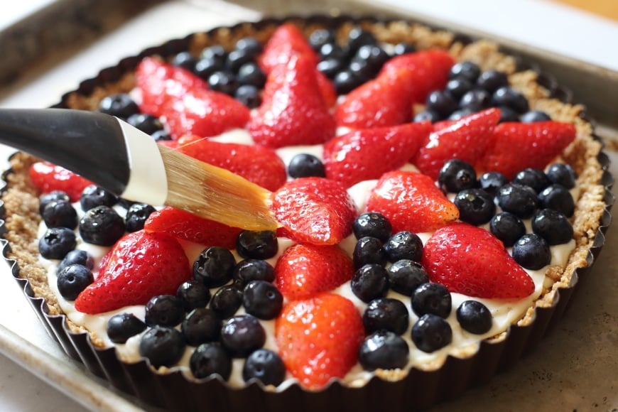 Process shot showing a pastry brush brushing apricot jam over the berry tart.