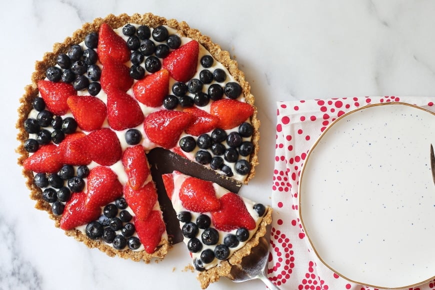 Overhead shot of berry tart, with a slice being removed. 