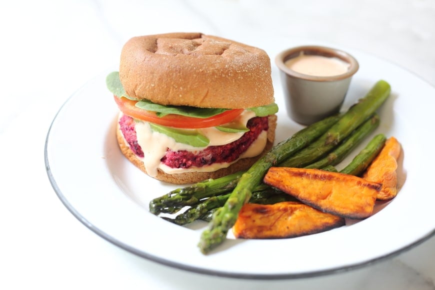 Gluten free veggie burger in bun on plate with roasted vegetables and sriracha mayo