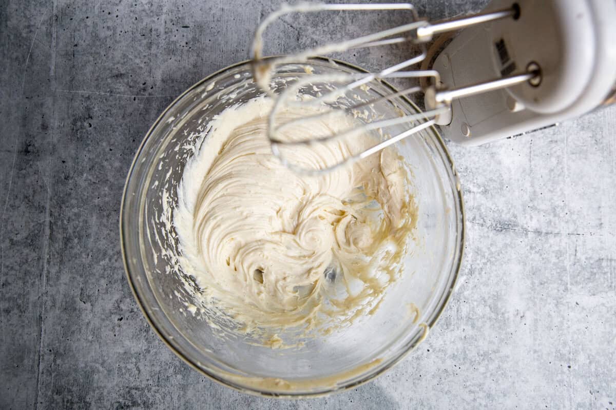 beating the creme fraiche and cream cheese in a bowl with an electric hand mixer