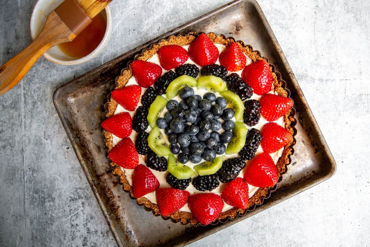 berries and fruit added to the top of the gluten-free tart which is resting on a baking sheet