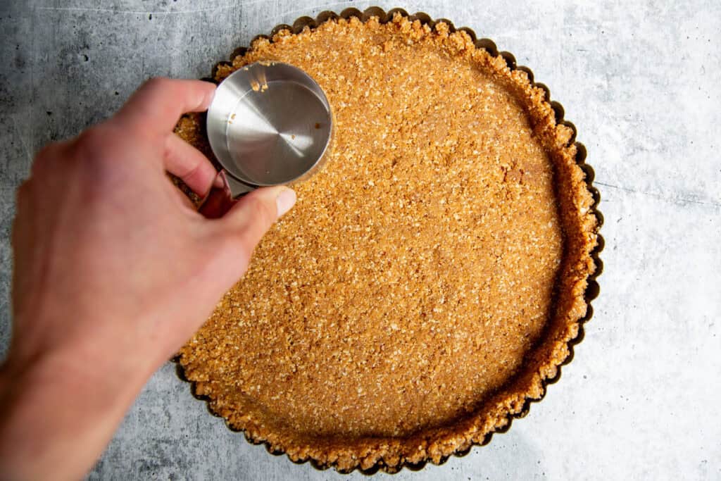 pressing the crust into a pie tin with the back of a measuring cup