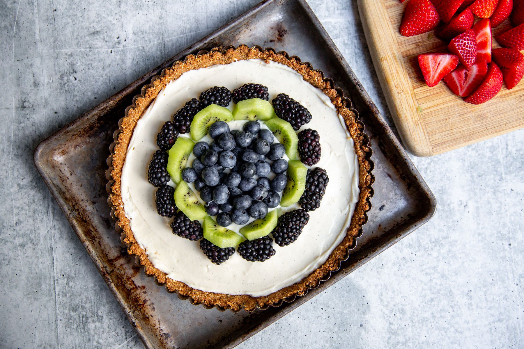 kiwi, blackberries, and blueberries added to the top of the gluten-free tart which is resting on a baking sheet