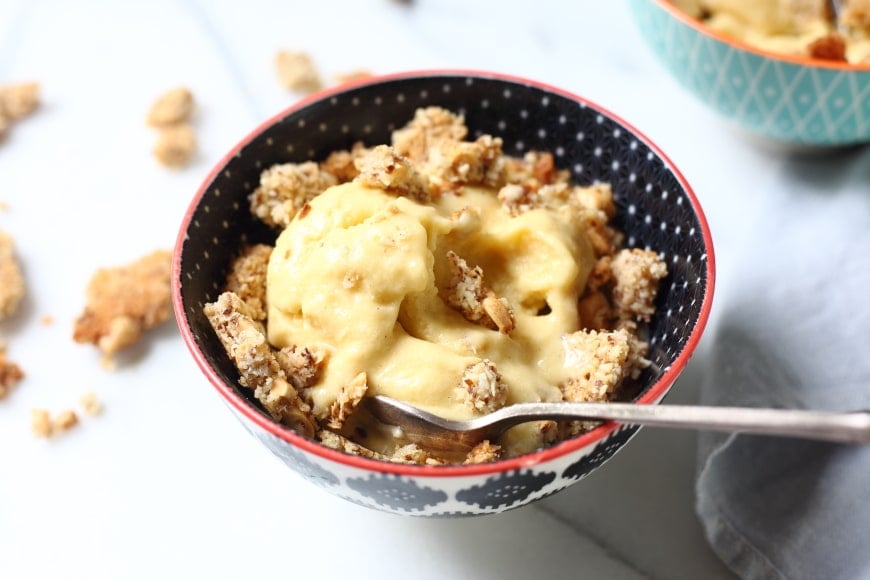 Vegan mango ice cream topped with coconut peanut crumble, in bowl with spoon