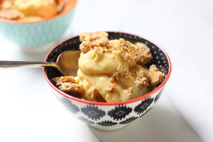 Side-shot of a bowl of vegan mango ice cream topped with coconut peanut crumble.