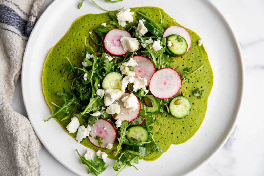 A chickpea flatbread toped with radishes, cucumbers, arugula, and feta cheese. 