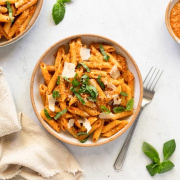 Tomato pesto pasta in a bowl, topped with basil and shaved parmesan cheese.