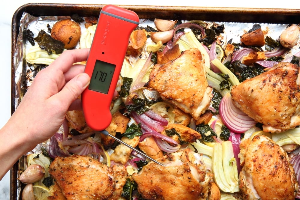 Sheet pan chicken thighs on pan with meat thermometer taking temperature