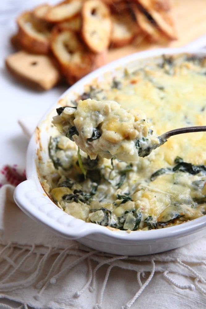 Close up of a spoon scooping out warm spinach and artichoke dip. 